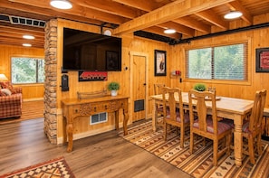 A wooden interior with a dining area, a fireplace, and a television. - Creekside Cabin by Cottonwood Lodging (Brighton)