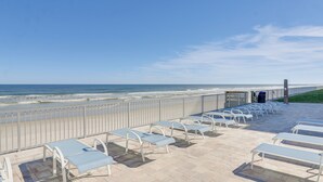 A beachside patio with rows of white lounge chairs and a metal railing overlooking the ocean. - Beautiful Condo with an Ocean View | Steps from Pool & Beach (New Smyrna Beach)