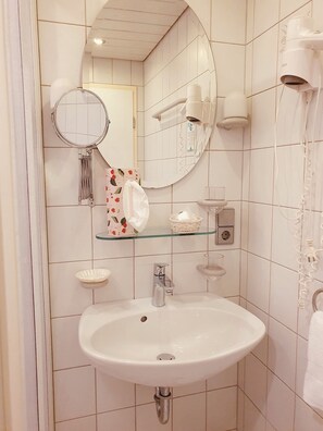 Casa de banho com uma pia branca, um espelho, um secador de cabelo e um porta-toalhas.