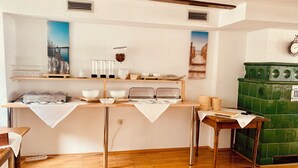 A kitchen area with a buffet setup, a green stove, and a wall-mounted clock. - Gasthof Sonne (Schiltach)