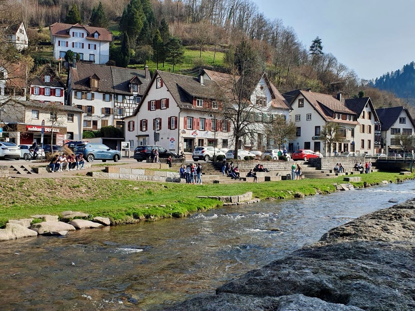 A riverside town with traditional buildings, a public seating area, and a bridge.