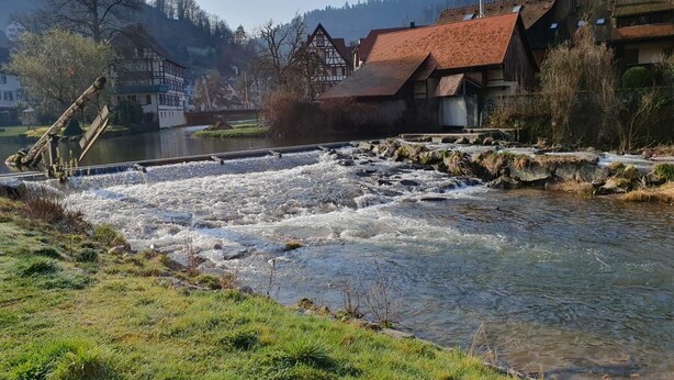 A river with a wooden structure, buildings with traditional architecture, and a mountainous backdrop. - Gasthof Sonne (Schiltach)