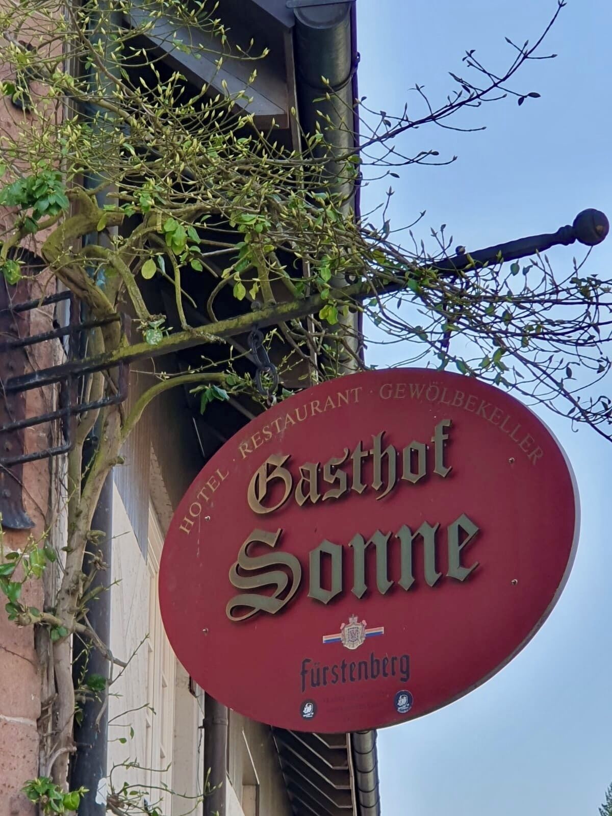 Un panneau rouge portant les inscriptions « Hotel Restaurant Gasthof Sonne » et « Furstenberg », indiquant la présence d’un hôtel et d’un restaurant.