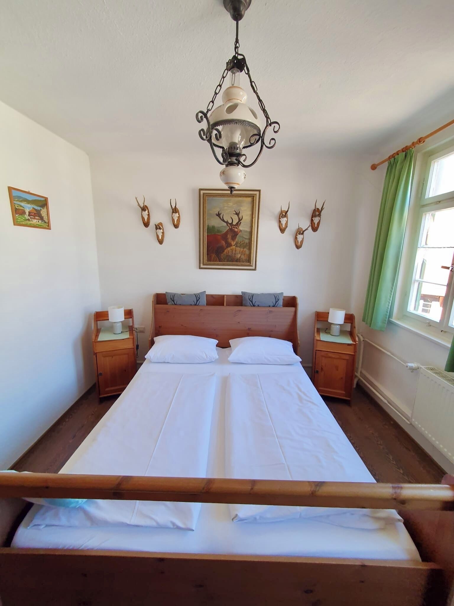 Une chambre à coucher avec un lit en bois, deux tables de chevet, un luminaire suspendu et des bois de cerf fixés au mur.