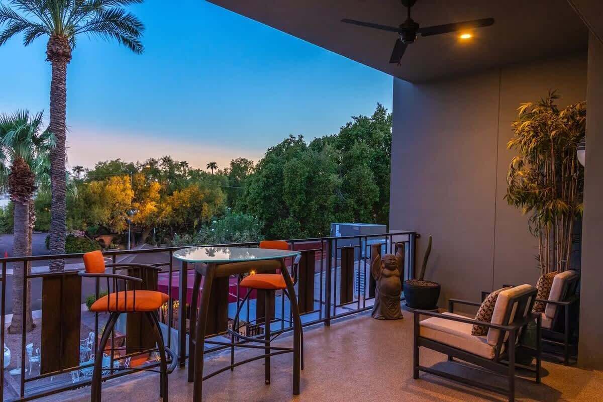 A balcony with outdoor seating, a ceiling fan, and a view of trees and a palm tree.