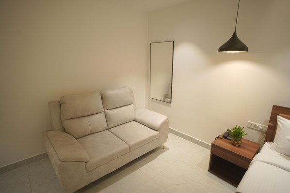 A modern living room with a beige sofa, a wooden nightstand with a plant, and a large mirror on the wall.