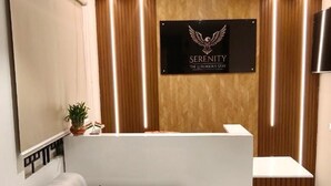 A reception area with a wooden reception desk, a white sofa with a brown cushion, and a wall-mounted sign. - Serenity the luxurious stay (Bengaluru)