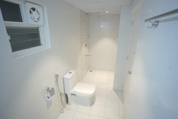 A compact bathroom with a toilet, a shower, and a window with a fan. - Serenity the luxurious stay (Bengaluru)