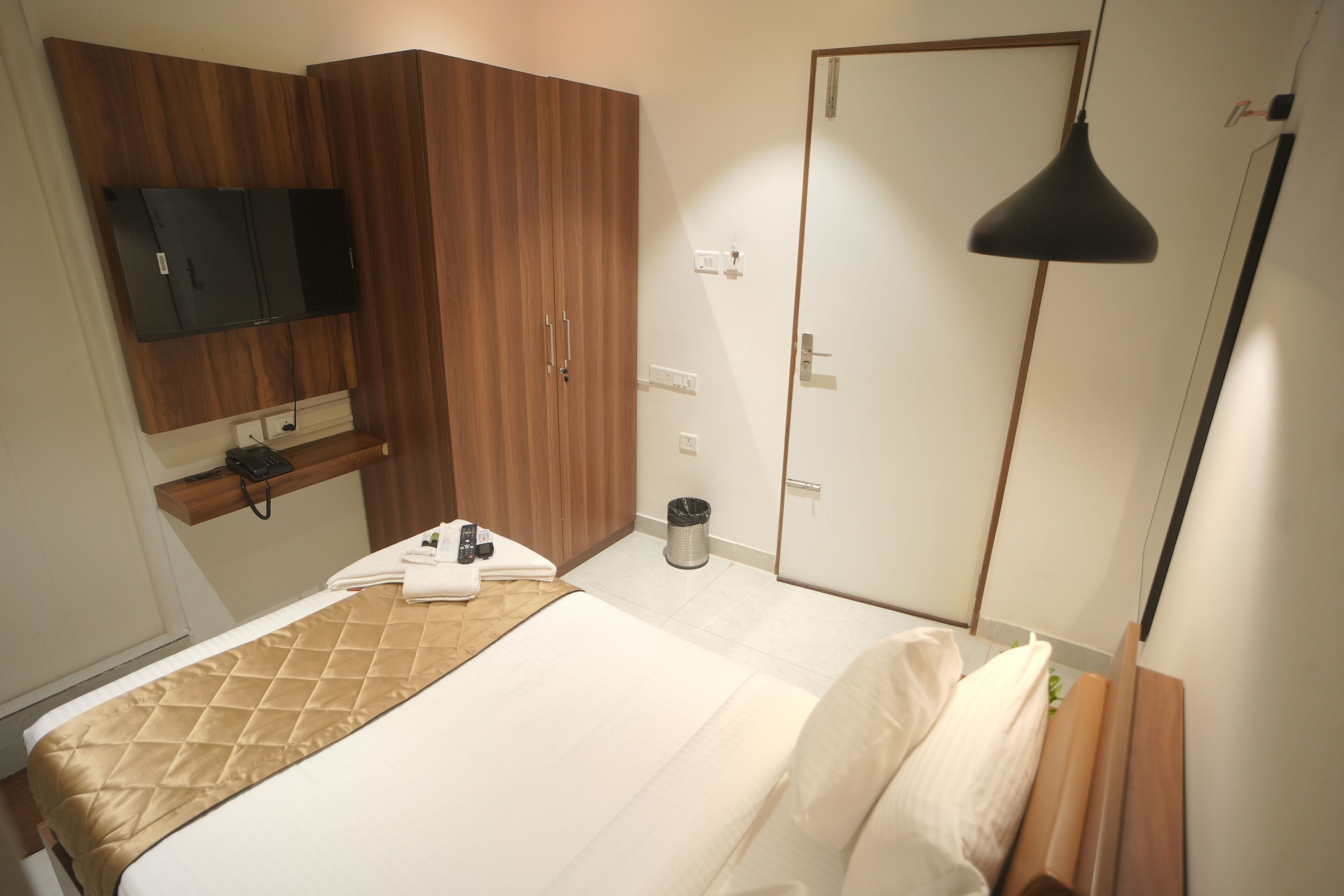 Habitación de hotel con cama, televisión montada en la pared, armario, mesita de noche y cubo de basura.