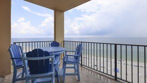 A balcony with a table and chairs, overlooking a beach with umbrellas and people. - Phoenix V 1202 1 Bedroom Condo (Orange Beach)