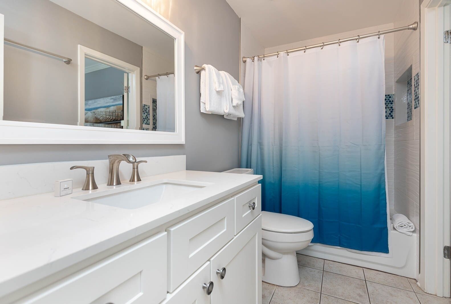 Een badkamer met een wit wastafelmeubel, twee wastafels, een toilet en een douche met een blauwe verloopgordijn.