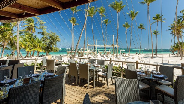 Ein Essbereich im Freien mit Korbmöbeln und Blick auf Strand und Meer.