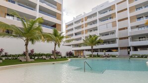 Ein modernes Hotel mit mehreren Balkonen, einem Swimmingpool und Palmen.