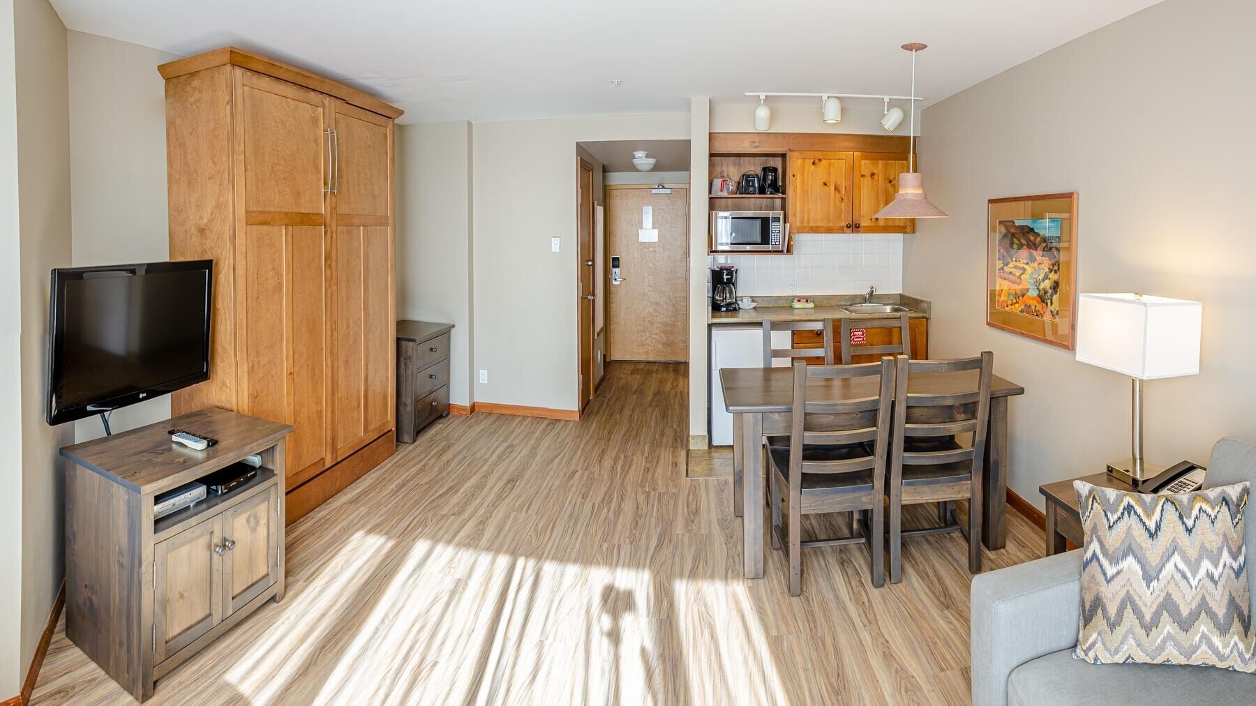 Un espacio habitable compacto con televisor, armarios de madera, zona de comedor y kitchenette.