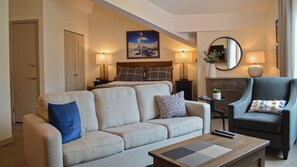 A hotel room with a sofa, armchair, coffee table, and a bed with a headboard.