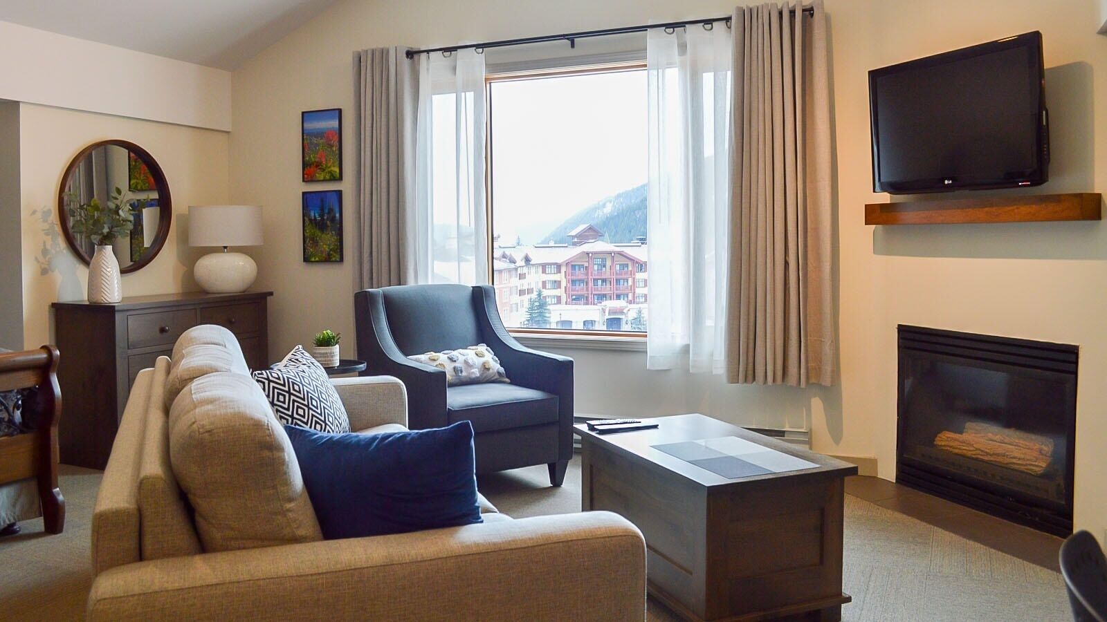 A living room with a sofa, armchair, coffee table, TV, fireplace, and a window with curtains.