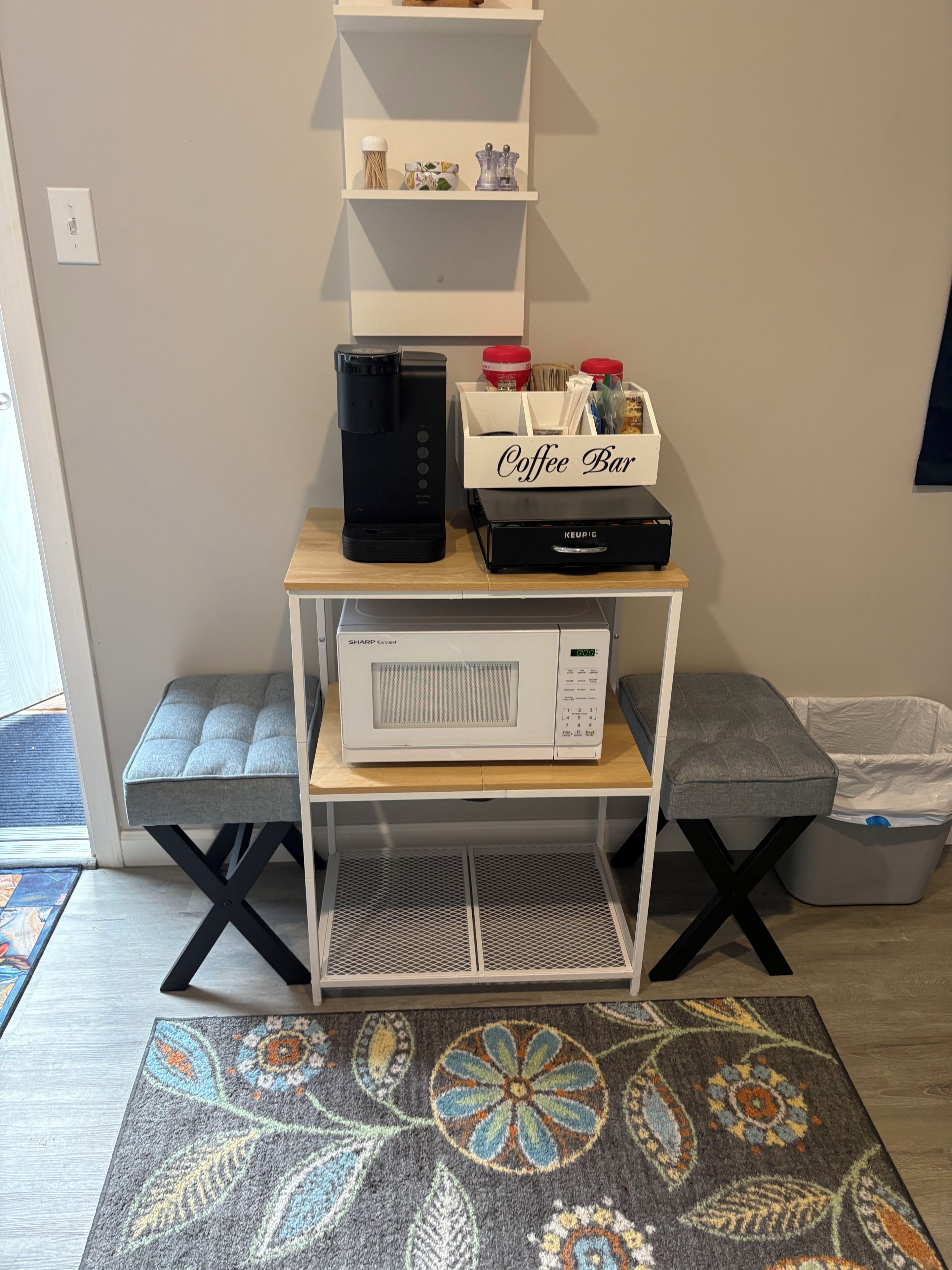 A kitchenette with a coffee maker, microwave, and storage box labeled 'Coffee Bar' on a wooden table.