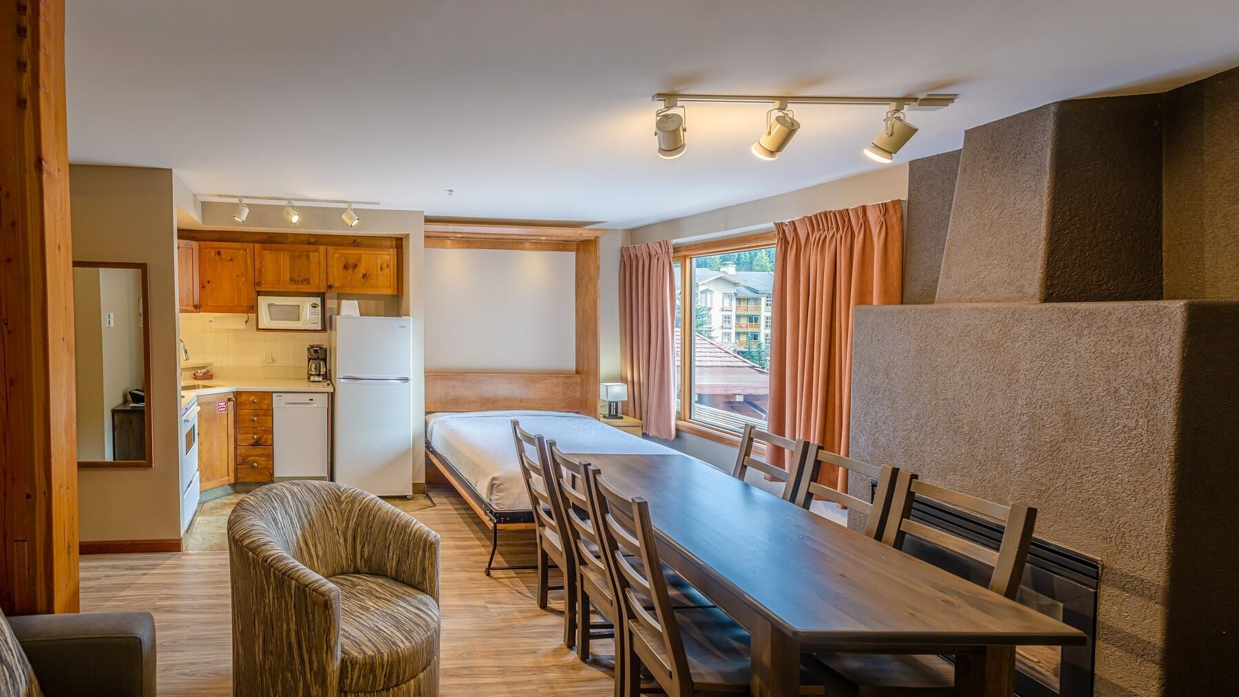 A compact hotel room with a kitchenette, a dining area, and a large window offering a view of buildings.