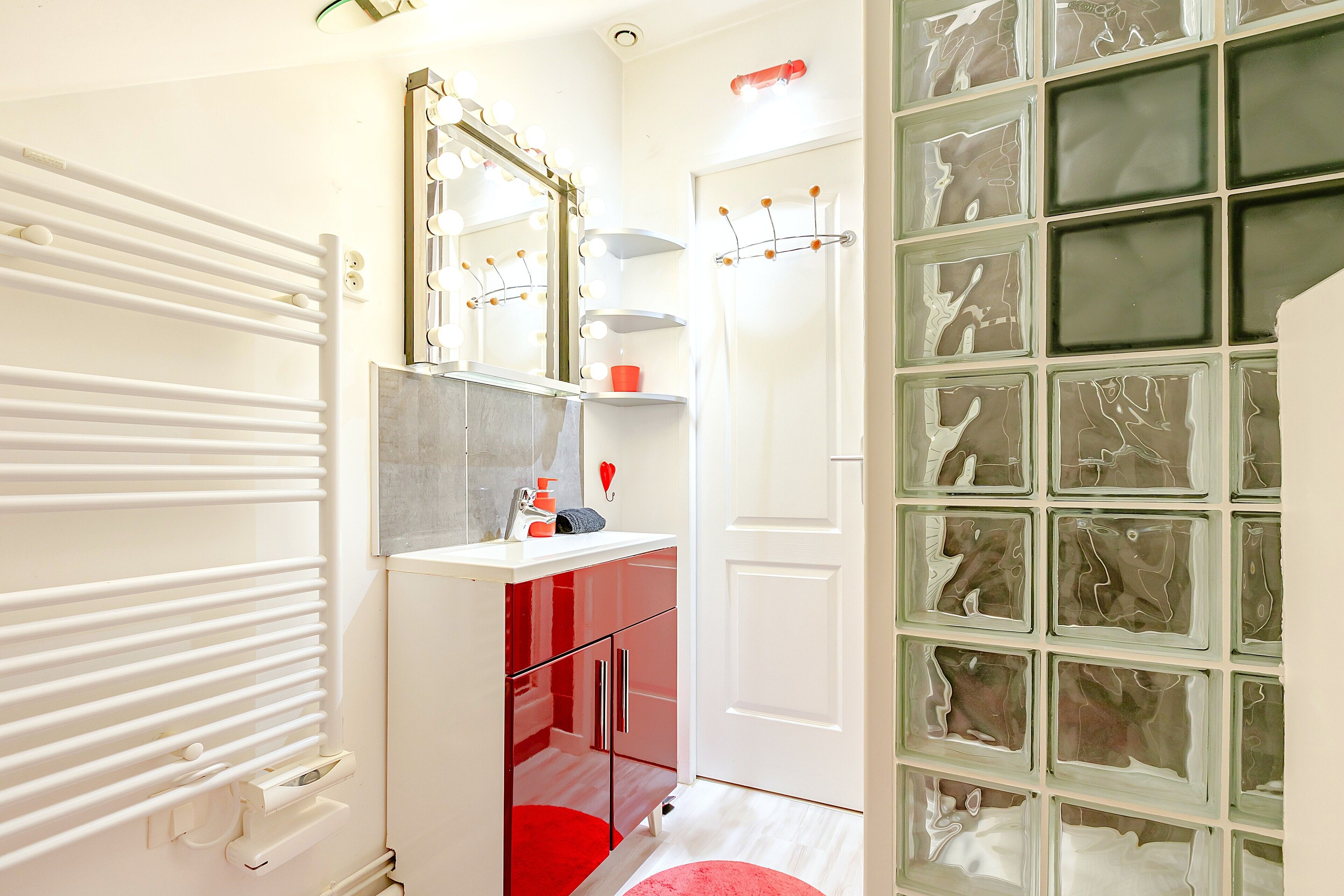 A bathroom with a white radiator, a vanity with a mirror, and a red bath mat.