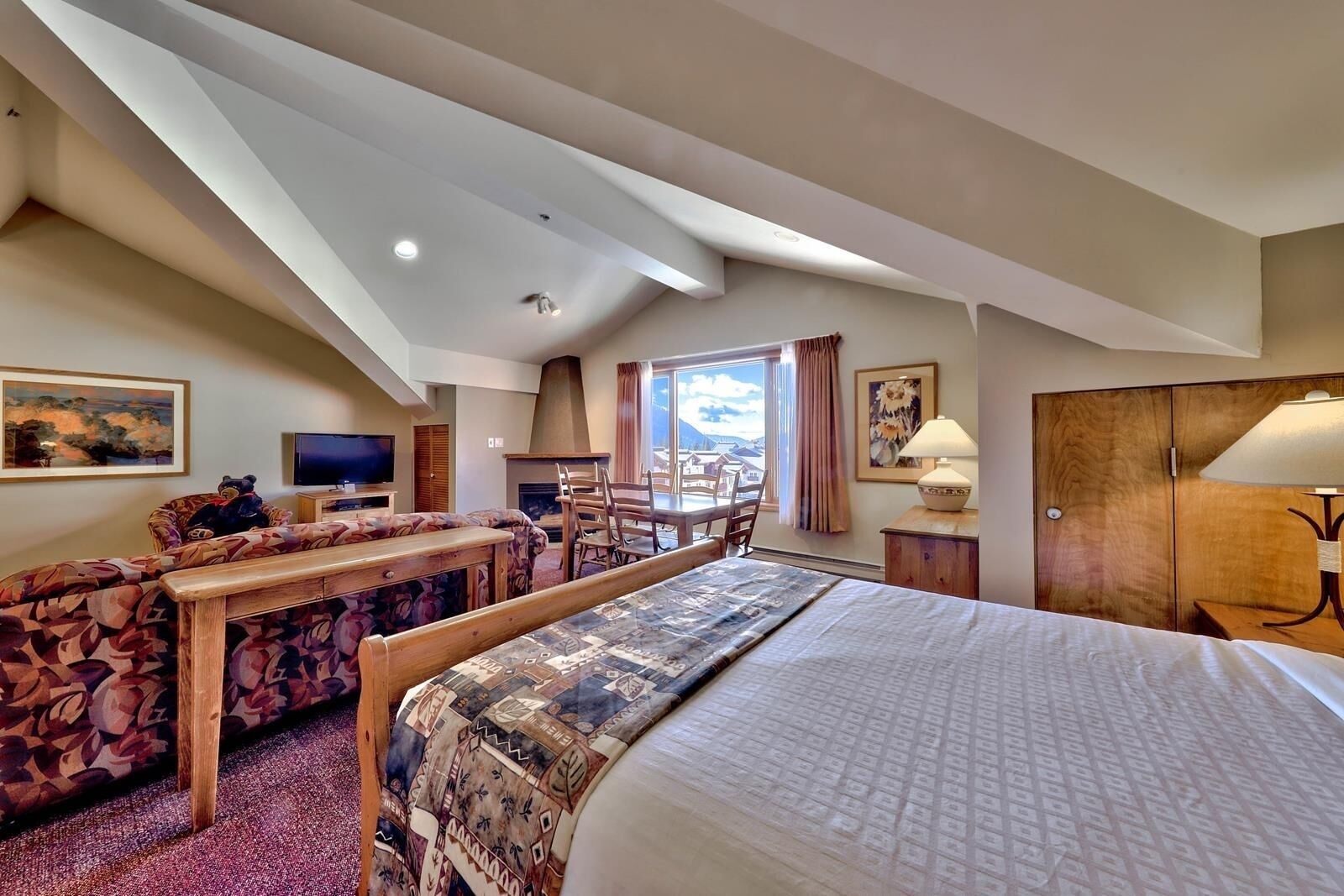 A hotel room with a large bed, a sofa, a dining table, and a fireplace.