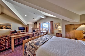A hotel room with a large bed, a sofa, a dining table, and a fireplace. - Cahilty #460 Hotel Room (Sun Peaks)