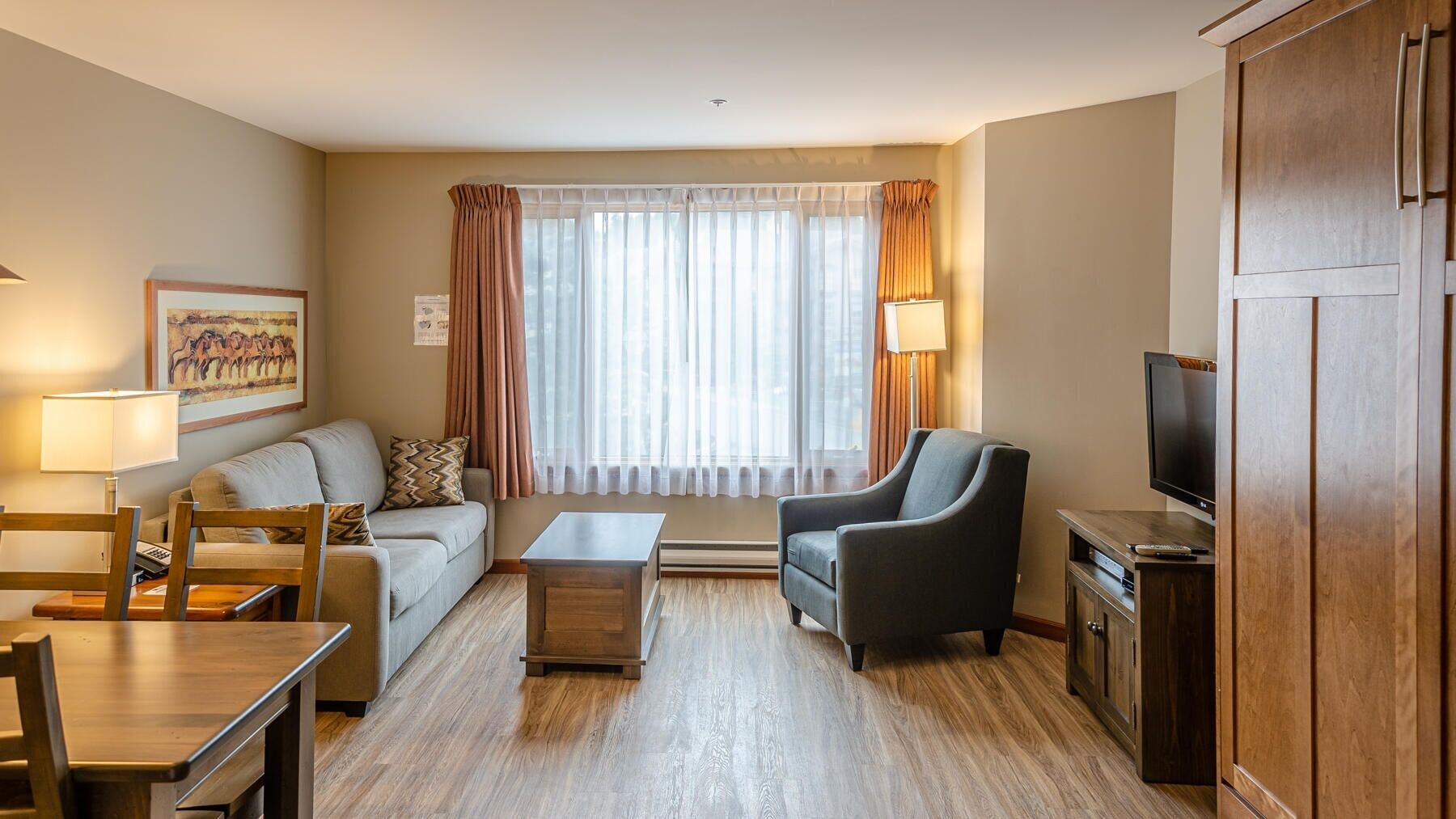 Una sala de estar moderna con sofá, sillón, mesa de centro, televisor y suelo de madera.