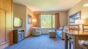 A hotel room with a TV, a sofa, a dining table, and a window with curtains.