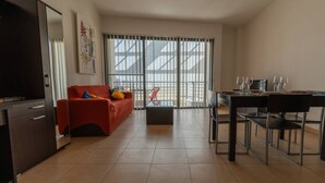 A modern living room with a red sofa, a dining table with chairs, and a kitchen area. - The King at Roulette Modern Apartment Paceville (St. Julian's)