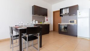 A modern kitchen with dark cabinets, a dining table with chairs, a microwave, and a refrigerator. - The King at Roulette Modern Apartment Paceville (St. Julian's)