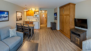 A compact living space with a kitchenette, a dining area, a sofa, a television, and a wardrobe.