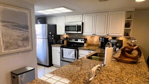 A kitchen with white cabinets, stainless steel appliances, granite countertops, and a painting on the wall. - Nothing Between You & The Beach 2 Bedroom Condo (South Padre Island)
