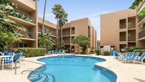 A pool area with blue water, surrounded by lounge chairs and palm trees. - Nothing Between You & The Beach 2 Bedroom Condo (South Padre Island)