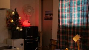 Een kleine keuken met een koelkast, een kerstboom en een ventilator.
