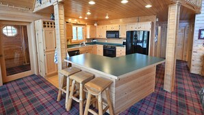 A wooden cabin interior with a central island, bar stools, wooden cabinets, and a plaid floor. - Loon Song On Lost Land Lake 4 Bedroom Home (Hayward)