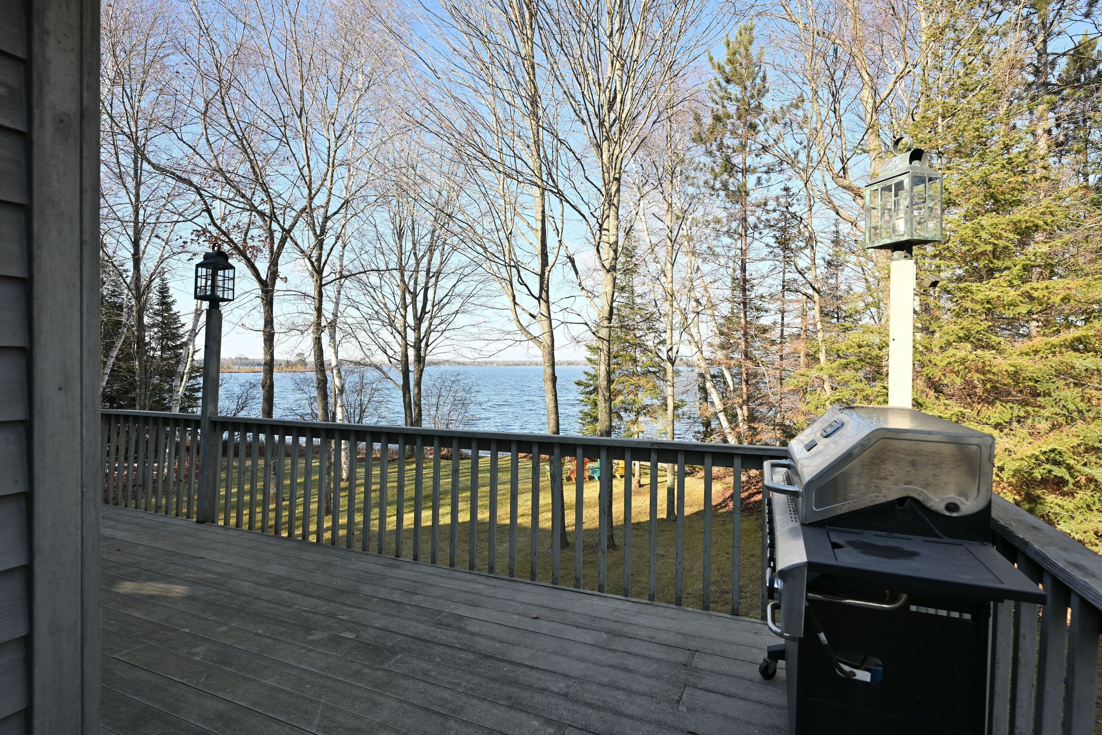Eine Terrasse mit Grill und Blick auf einen von Bäumen umgebenen See.