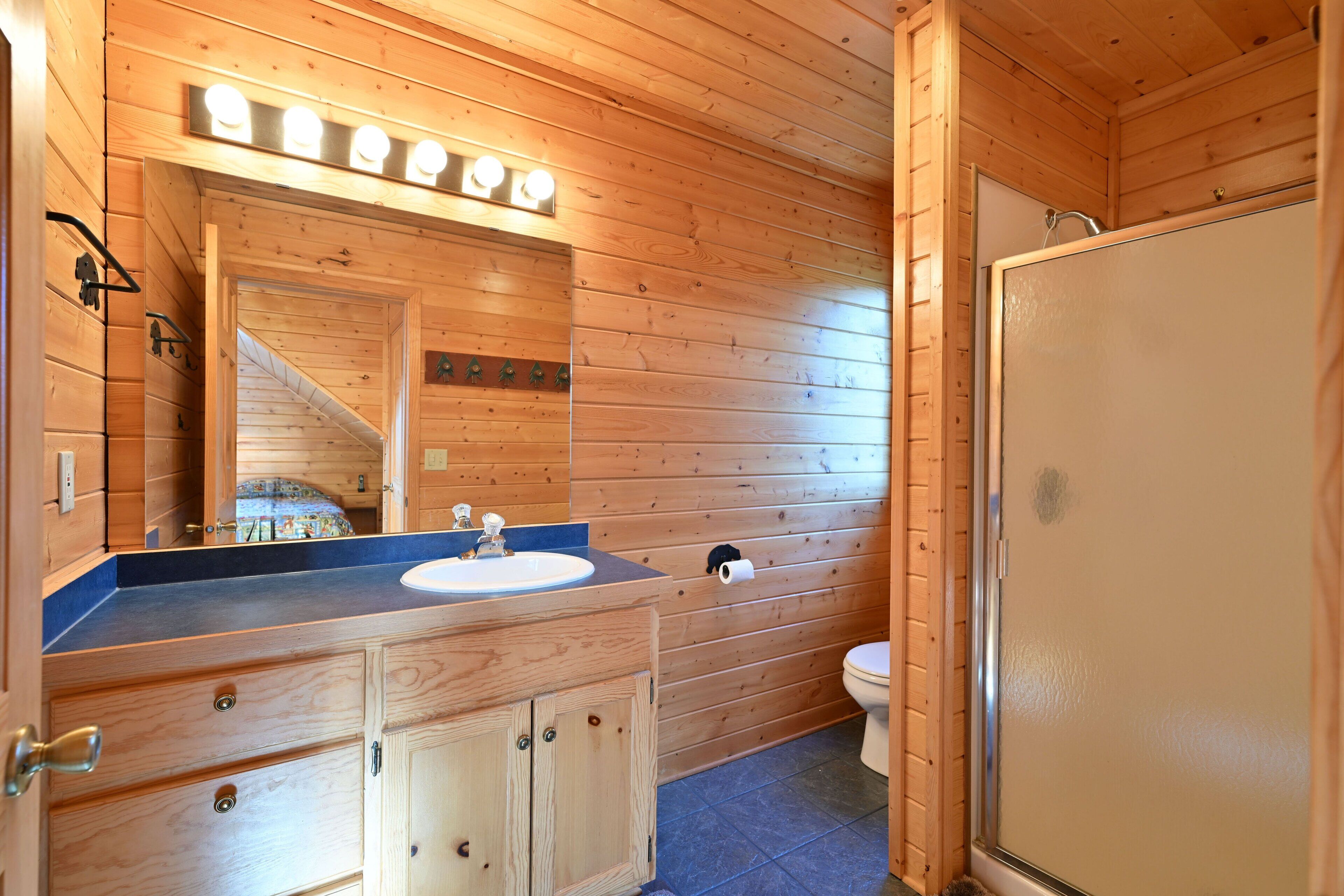 Un baño de cabaña de madera con lavamanos, espejo y retrete.