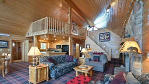 A cozy log cabin interior with a living room, kitchen, and a staircase leading to an upper deck. - Loon Song On Lost Land Lake 4 Bedroom Home (Hayward)