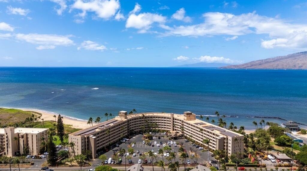 A hotel with a curved building, a parking lot, and a beach view.