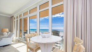 A room with a round table and chairs, large windows with a view of the sea, and a balcony with outdoor furniture. - Phoenix Gulf Towers 302 2 Bedroom Condo (Orange Beach)
