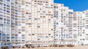Un edificio residencial de varios pisos con balcones, un espacio al aire libre techado con asientos y un cielo azul despejado.