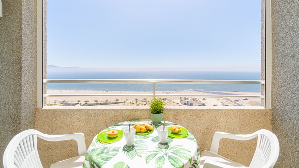Un balcón con una mesa lista para dos personas, con vista a la playa.