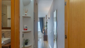 Un pasillo con puerta de madera, pared blanca y suelo de baldosas.