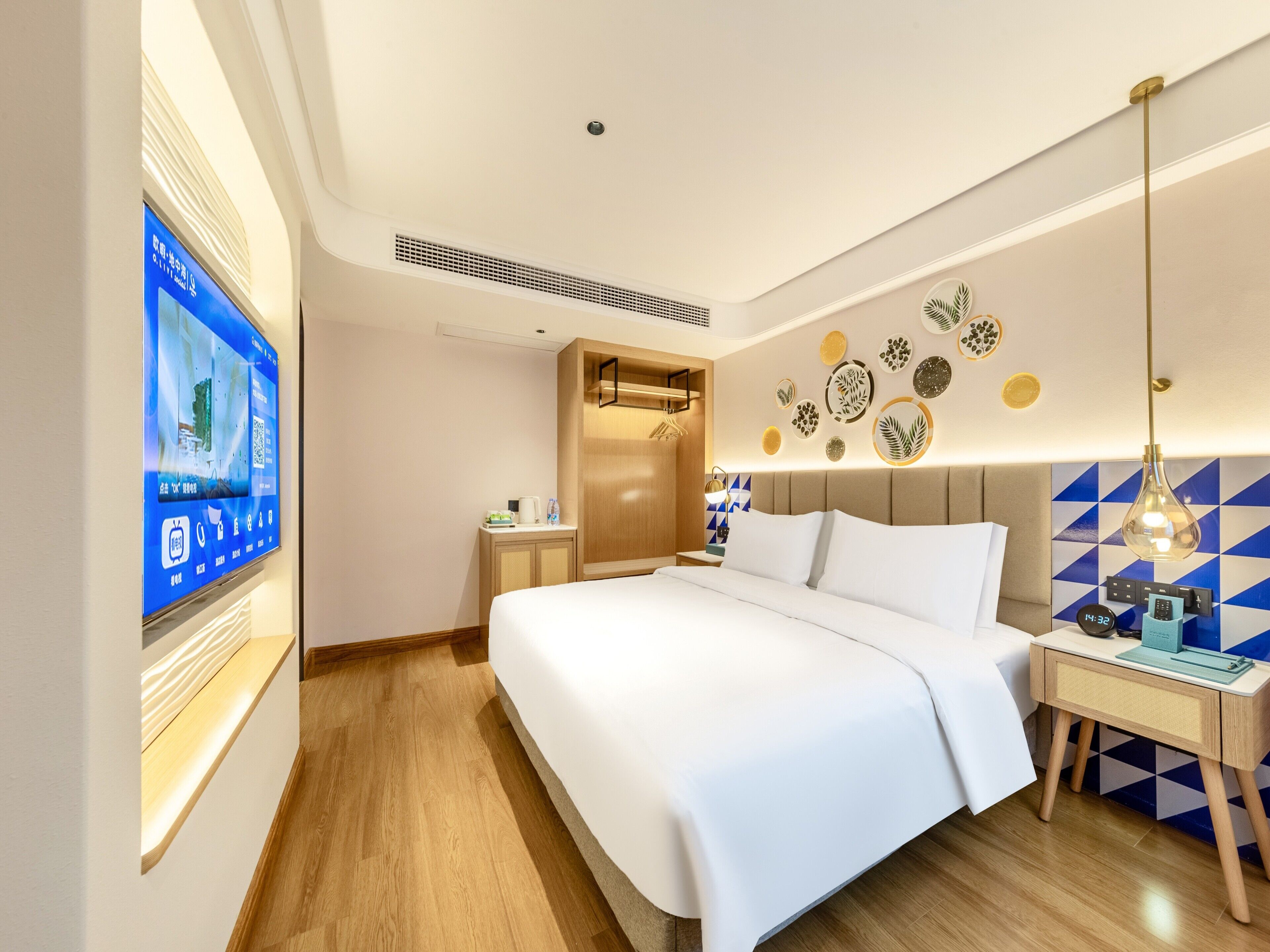 A modern hotel room with a large bed, a bedside table with a lamp, a wall-mounted TV, and decorative wall art.