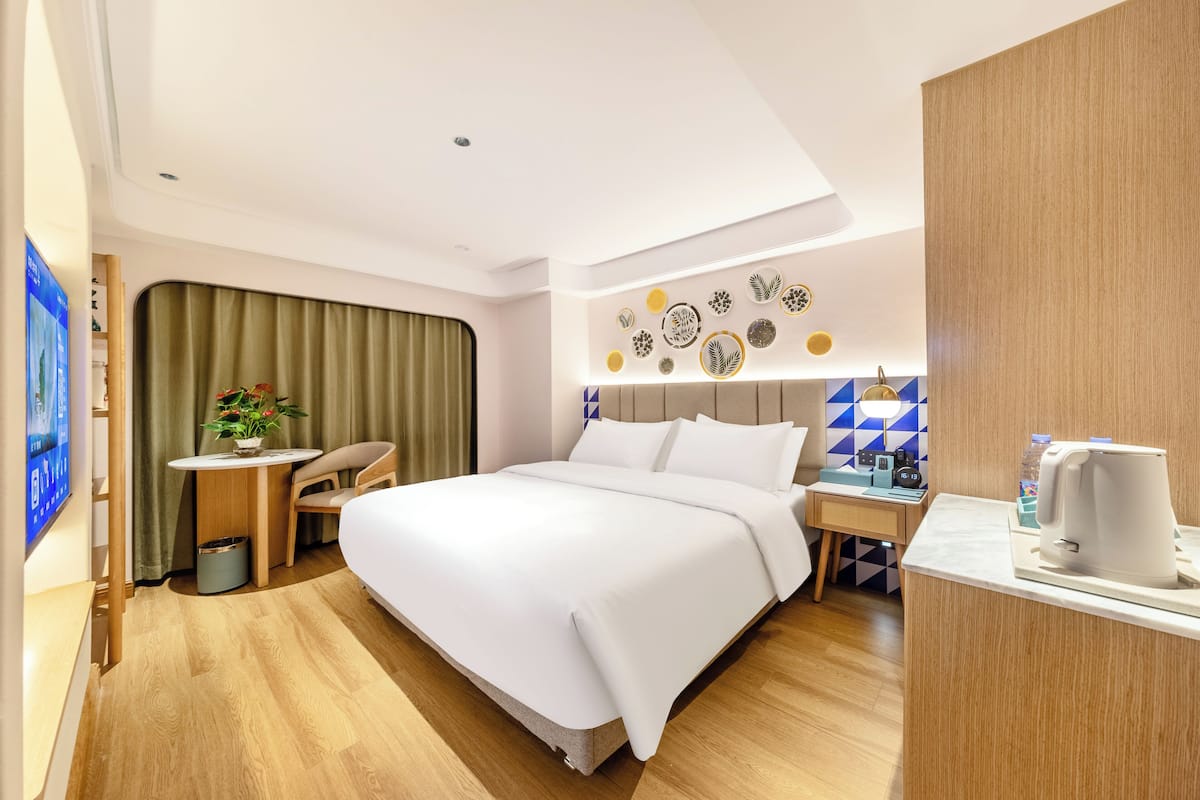 Una habitación de hotel moderna con una cama grande, un escritorio pequeño, una cafetera y un televisor en la pared.