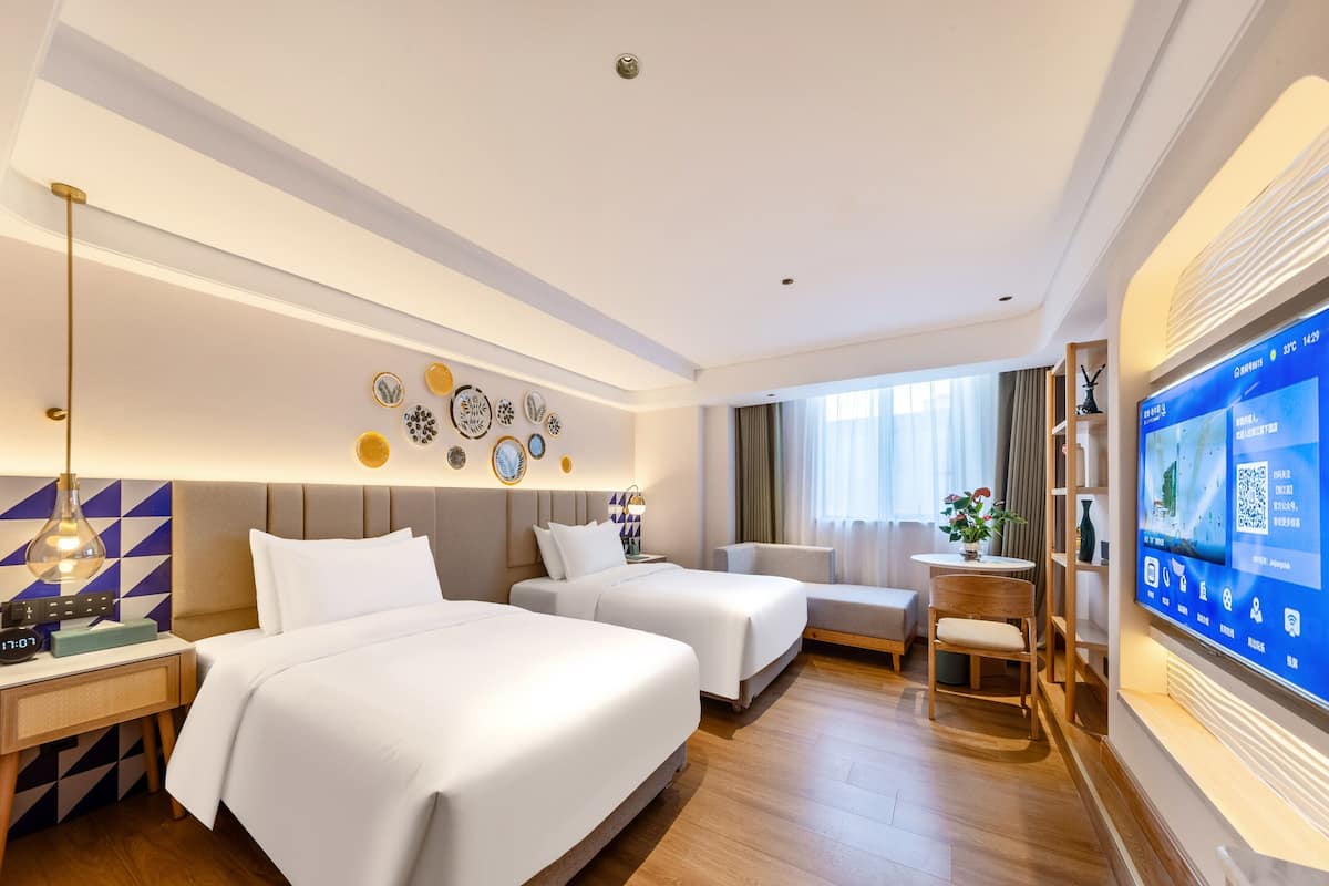 Habitación de hotel con dos camas, un escritorio, una silla, un televisor y decoración en la pared.