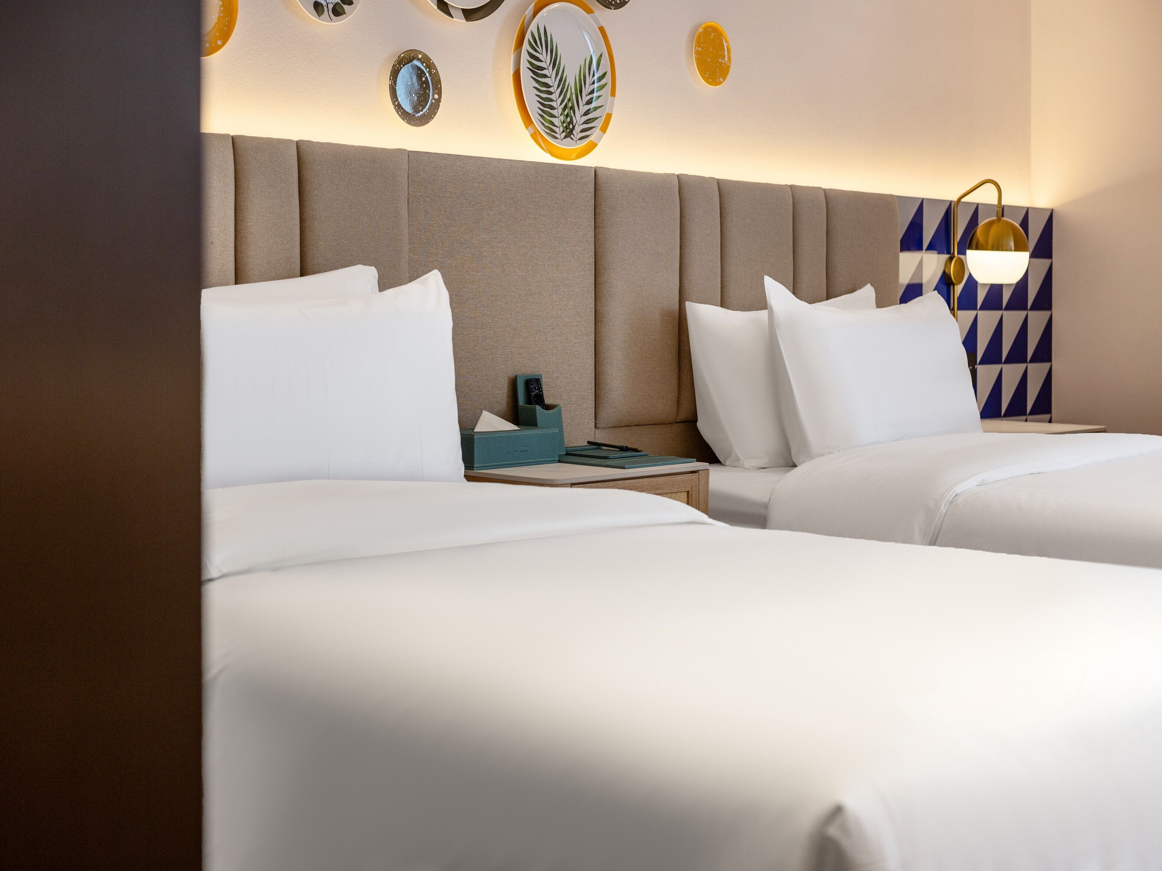A hotel room with two beds, a nightstand, and a wall with decorative plates and a geometric pattern.