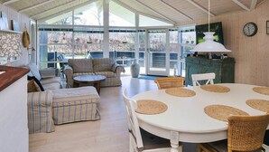 Una habitación amplia con techo alto, ventanas grandes, una mesa de comedor con individuales tejidos, mobiliario tapizado a rayas y un aparador de madera rústica.