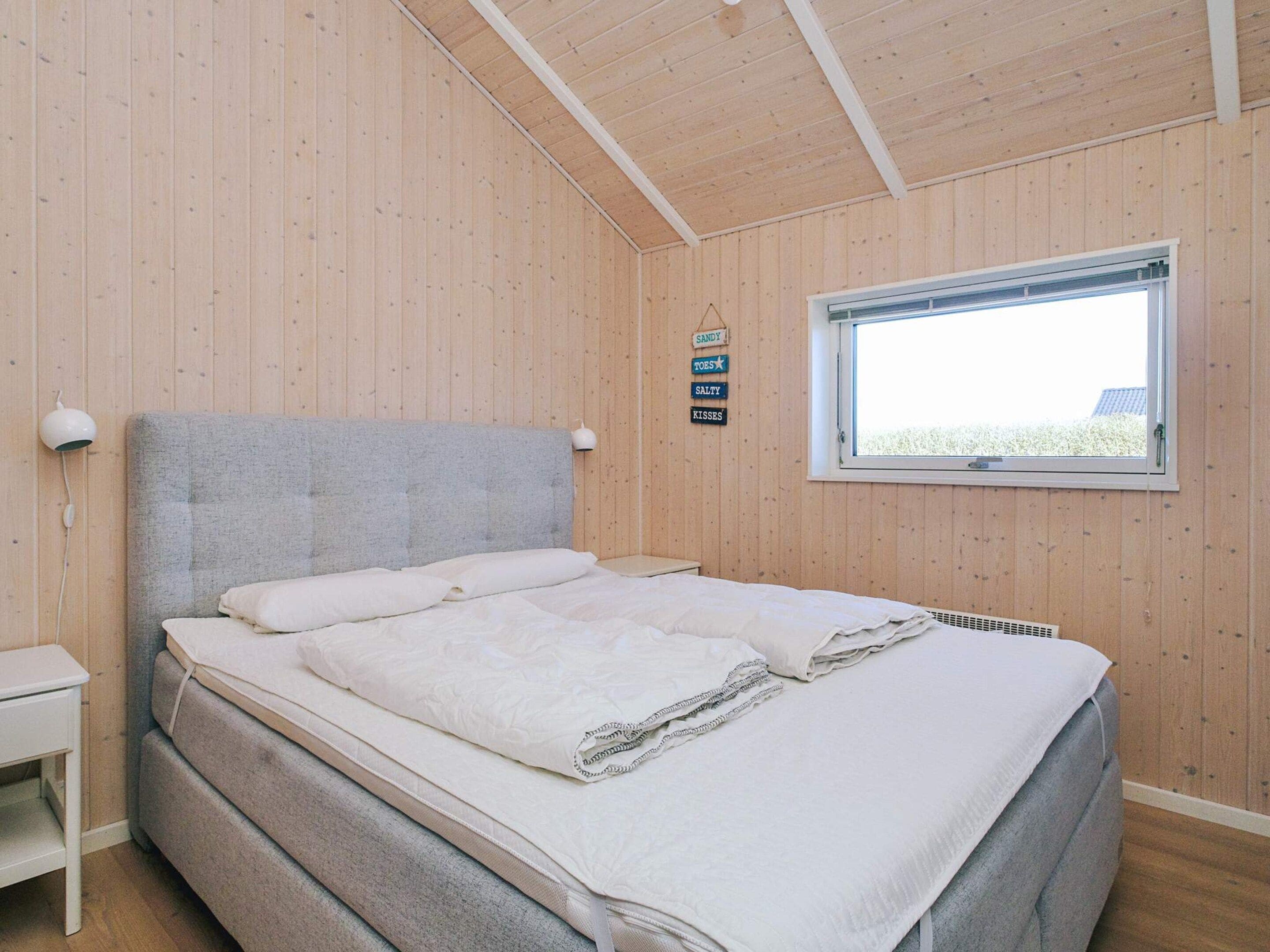 A bedroom with a bed, a bedside table, a window, and a wall-mounted sign.