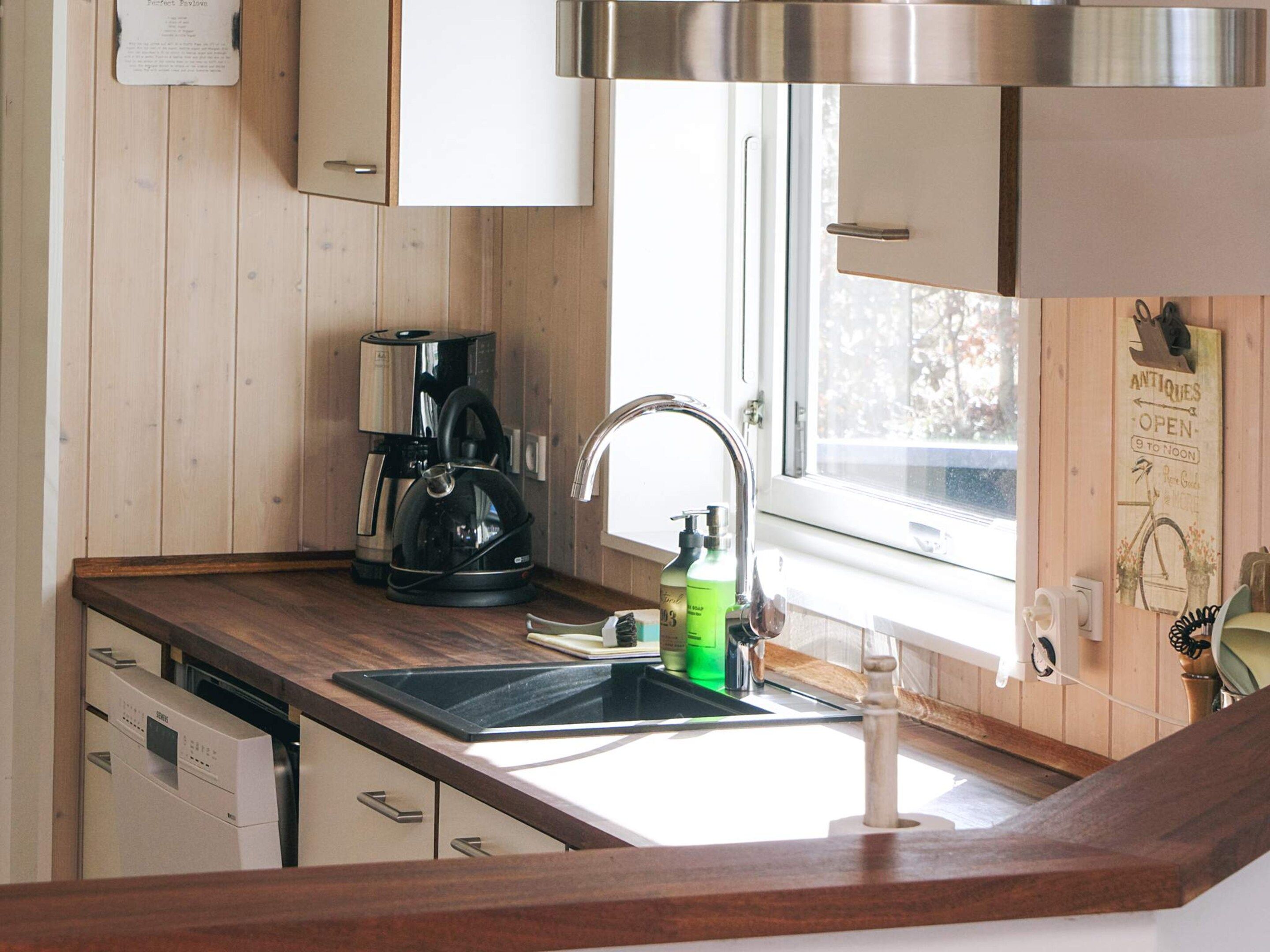 Una cocina con extractor de acero inoxidable, cafetera, hervidor y pileta con grifo.
