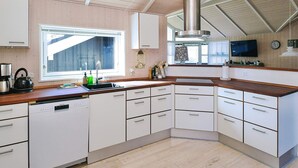 Una cocina moderna con armarios blancos, campana extractora de acero inoxidable, lavavajillas y ventana con persianas.